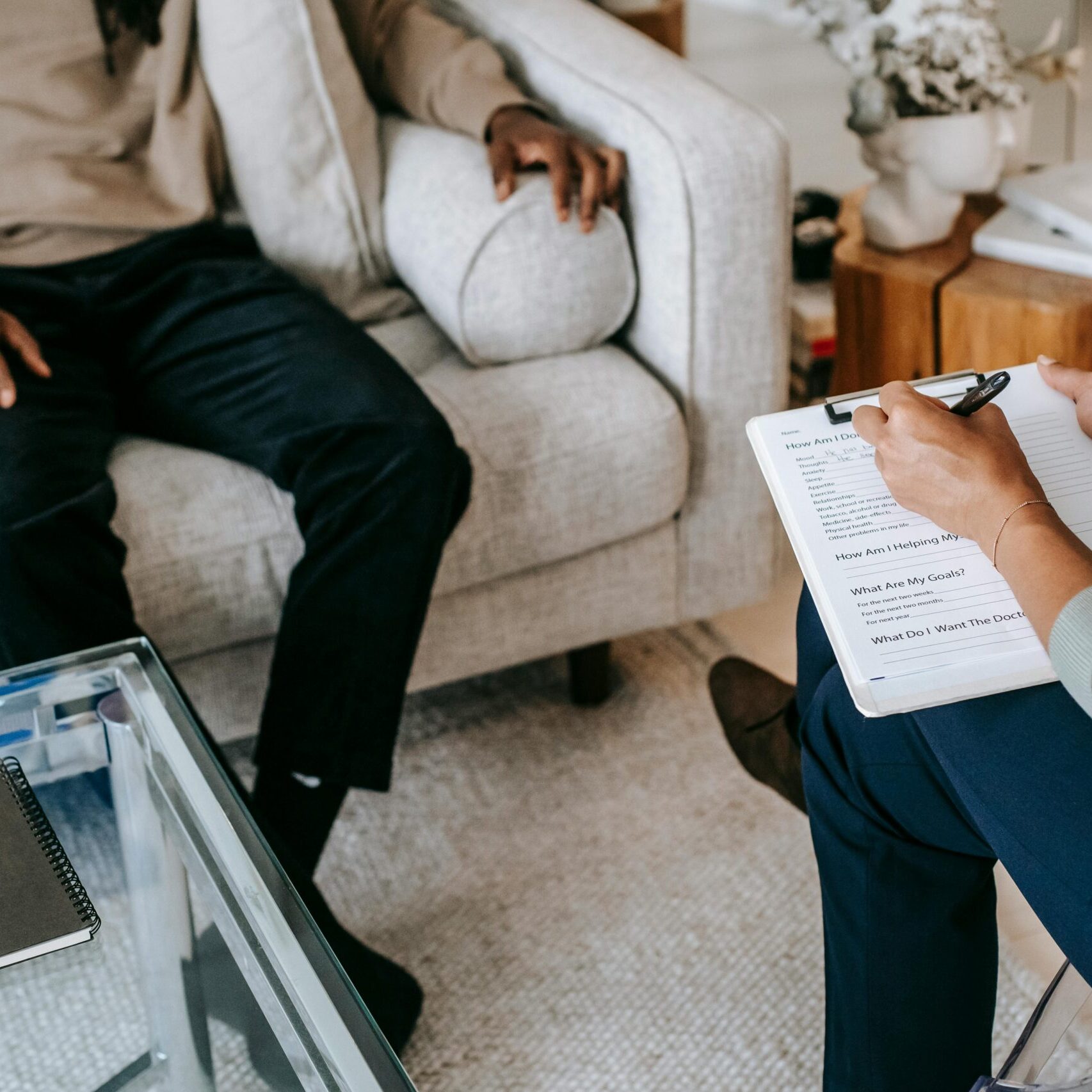 From above crop African American male in casual clothes sitting on comfy couch and answering professional female consultant questions in modern psychotherapy office