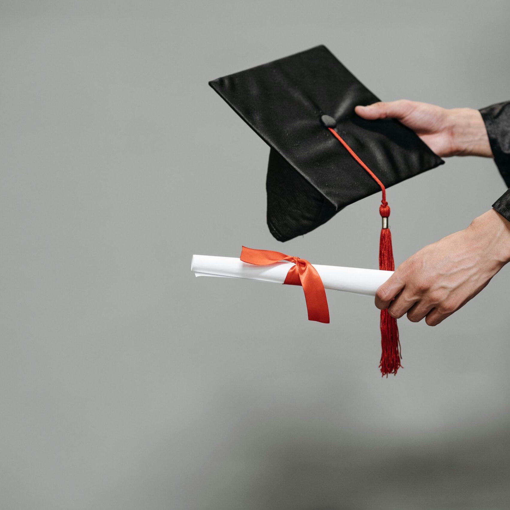Close-up of graduate holding cap and diploma with red ribbon, symbolizing success.